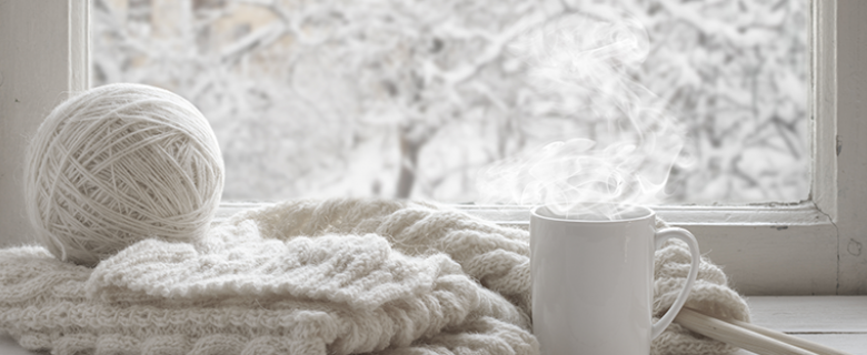 Varm kaffe i kop, med hvidt garn og strik sweater i en vindueskarm